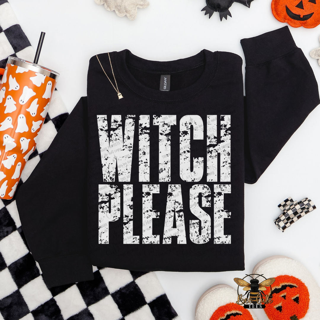 A black crewneck sweatshirt with 'WITCH PLEASE' printed in distressed white block letters, styled in a flat lay with Halloween-themed props including a ghost-patterned tumbler, black-and-white checkered fabric, and orange jack-o'-lantern decorations.