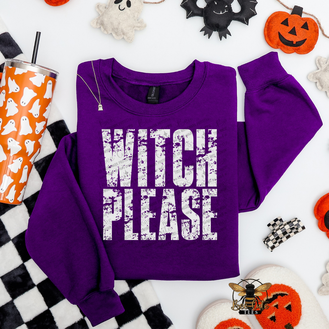 A purple crewneck sweatshirt with the words 'WITCH PLEASE' printed in a distressed white font across the front. The sweatshirt is presented in a flat-lay arrangement with Halloween-themed props including a patterned orange and white tumbler, a black and white checkered blanket, and small ghost and pumpkin decorations on a white background.