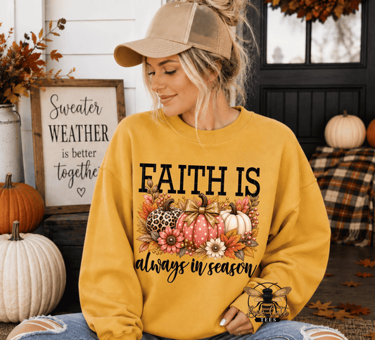 A woman wearing a mustard yellow crewneck sweatshirt with a 'FAITH IS always in season' autumn graphic, sitting in a fall-themed porch setting.