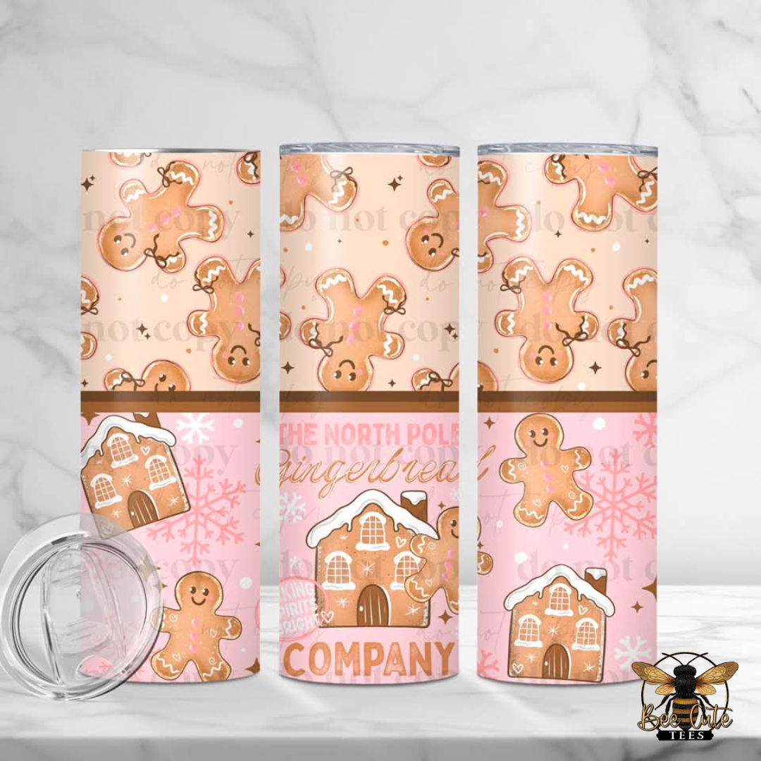 Three insulated tumblers with a festive gingerbread cookie and house pattern, shown on a light marble surface with a clear lid in the foreground.