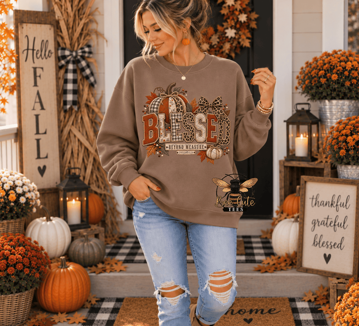 A woman modeling a brown crewneck sweatshirt with a large 'BLESSED' autumn graphic on the front, paired with distressed light blue jeans, standing on a decorated fall porch.