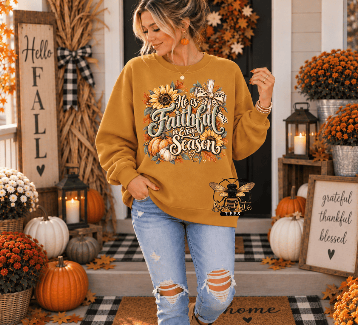 A woman stands on a decorated front porch wearing a mustard yellow graphic sweatshirt with autumn-themed text and illustrations, paired with light blue ripped jeans. The scene includes pumpkins, fall flowers, lanterns, and a 'Hello Fall' sign.