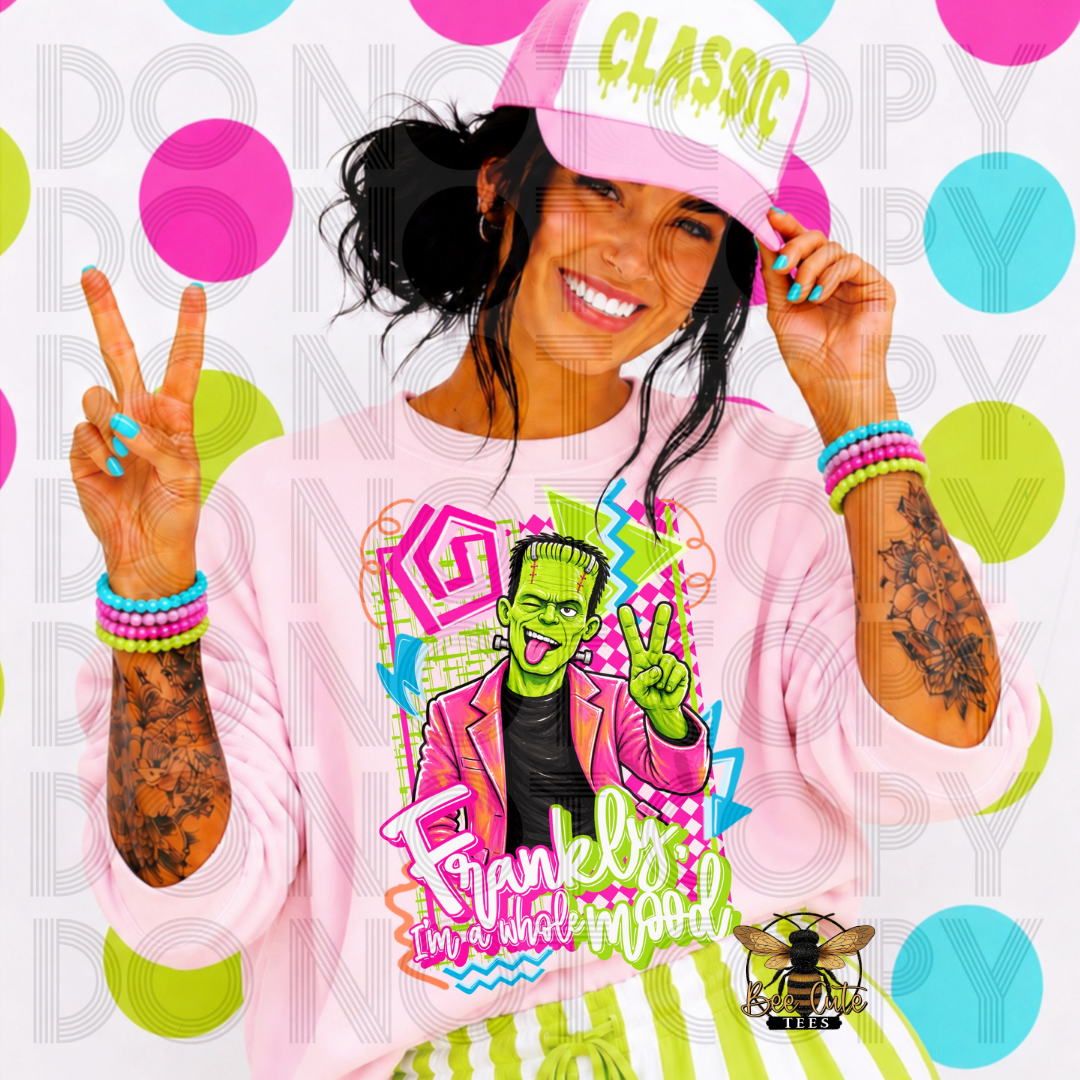 A woman wearing a light pink crewneck sweatshirt with a colorful Frankenstein graphic on the front, a matching pink cap with 'CLASSIC' in green, and striped green and white pants, posing against a white background with colorful polka dots.