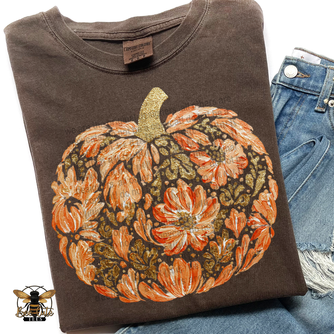 A folded dark brown t-shirt with a large orange and gold floral pumpkin graphic, styled next to a pair of blue jeans on a white background.
