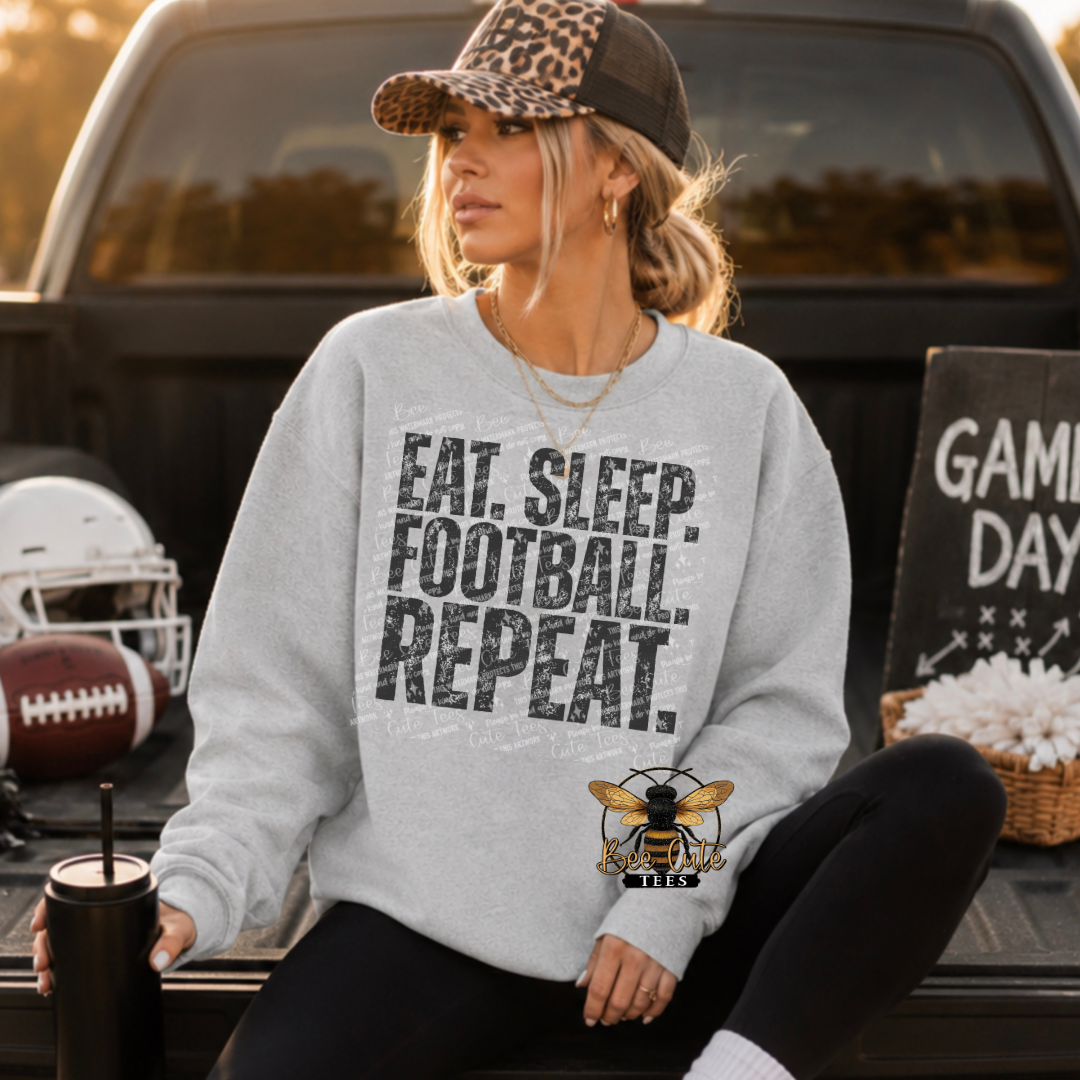 A woman sitting in the bed of a pickup truck wearing a light gray crewneck sweatshirt with the text 'EAT. SLEEP. FOOTBALL. REPEAT.'
