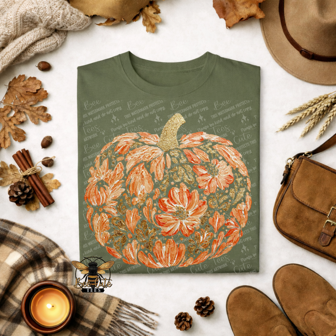 An olive green crewneck t-shirt featuring a large orange and gold floral pumpkin graphic, styled in a cozy autumn flat-lay with a hat, scarf, candle, and shoes.