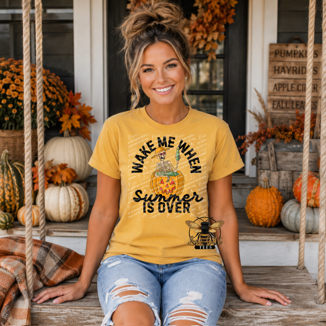 A woman sitting on a porch swing wearing a mustard yellow graphic t-shirt with a cartoon pumpkin and the text 'WAKE ME WHEN Summer IS OVER'.