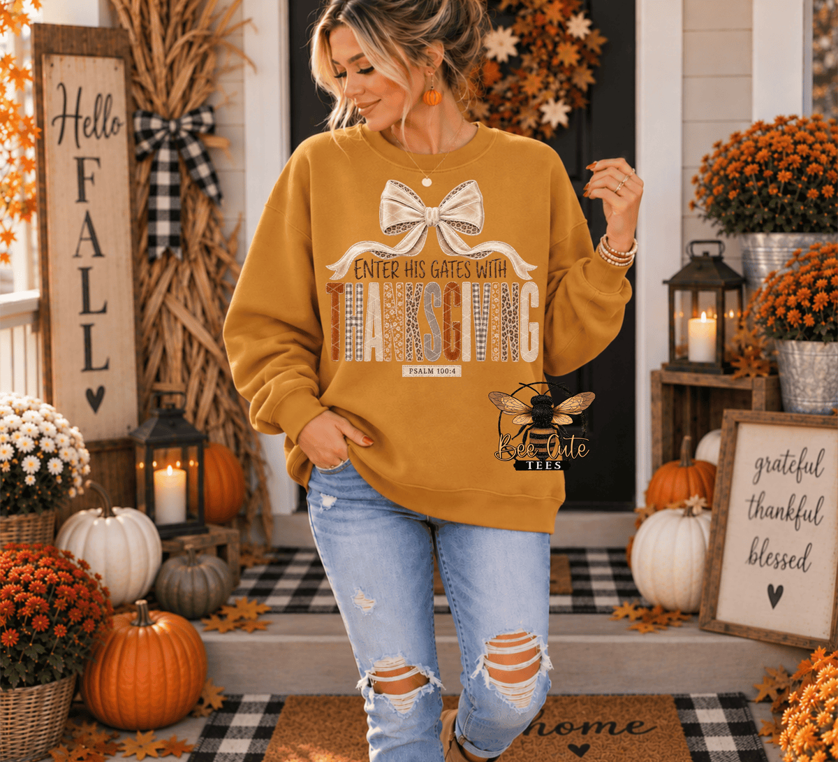 A woman modeling a mustard yellow graphic sweatshirt with a 'Thanksgiving' bow and bee logo, paired with distressed blue jeans, standing on a decorated autumn front porch.