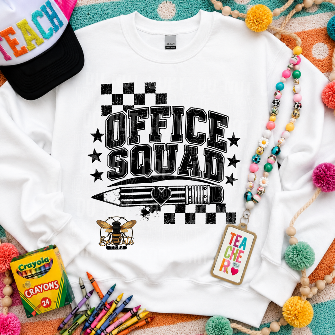 A white crewneck sweatshirt laid flat with a black 'OFFICE SQUAD' graphic featuring stars, a pencil, and a bee. The sweatshirt is styled with a colorful 'TEACH' cap, a beaded necklace, a 'TEACHER' tag, crayons, and a box of Crayola crayons on a patterned background.