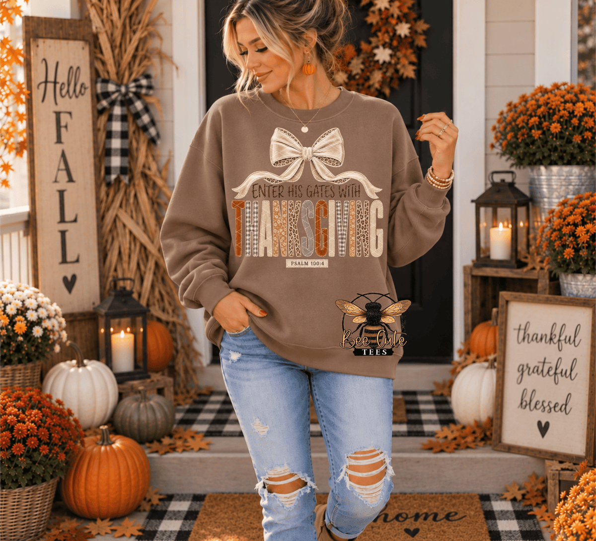 A woman stands on a decorated front porch wearing a taupe brown graphic sweatshirt with a bow and 'Thanksgiving' print, paired with distressed light blue jeans.