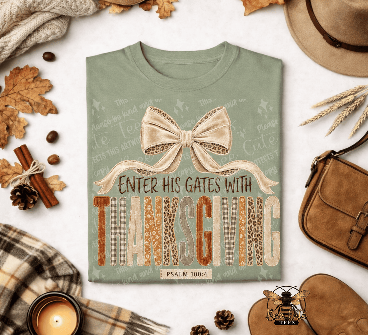 A sage green graphic t-shirt featuring a Thanksgiving-themed design with a large bow and the text 'ENTER HIS GATES WITH THANKSGIVING' and 'PSALM 100:4'. The shirt is presented in a styled flat-lay arrangement with autumn props including a candle, plaid scarf, hat, and leather bag on a white background.