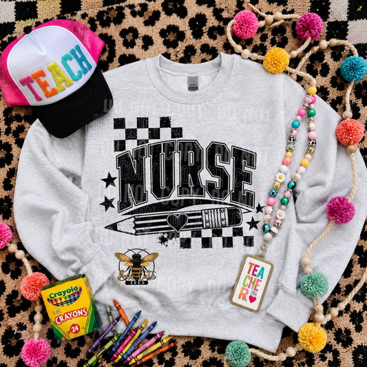 A light heather gray crewneck sweatshirt with a black graphic reading 'NURSE' over a pencil and checkerboard design, styled in a flat lay with a pink and black 'TEACH' trucker hat, crayons, a beaded necklace, a bee patch, and pom-poms on a leopard-print background.