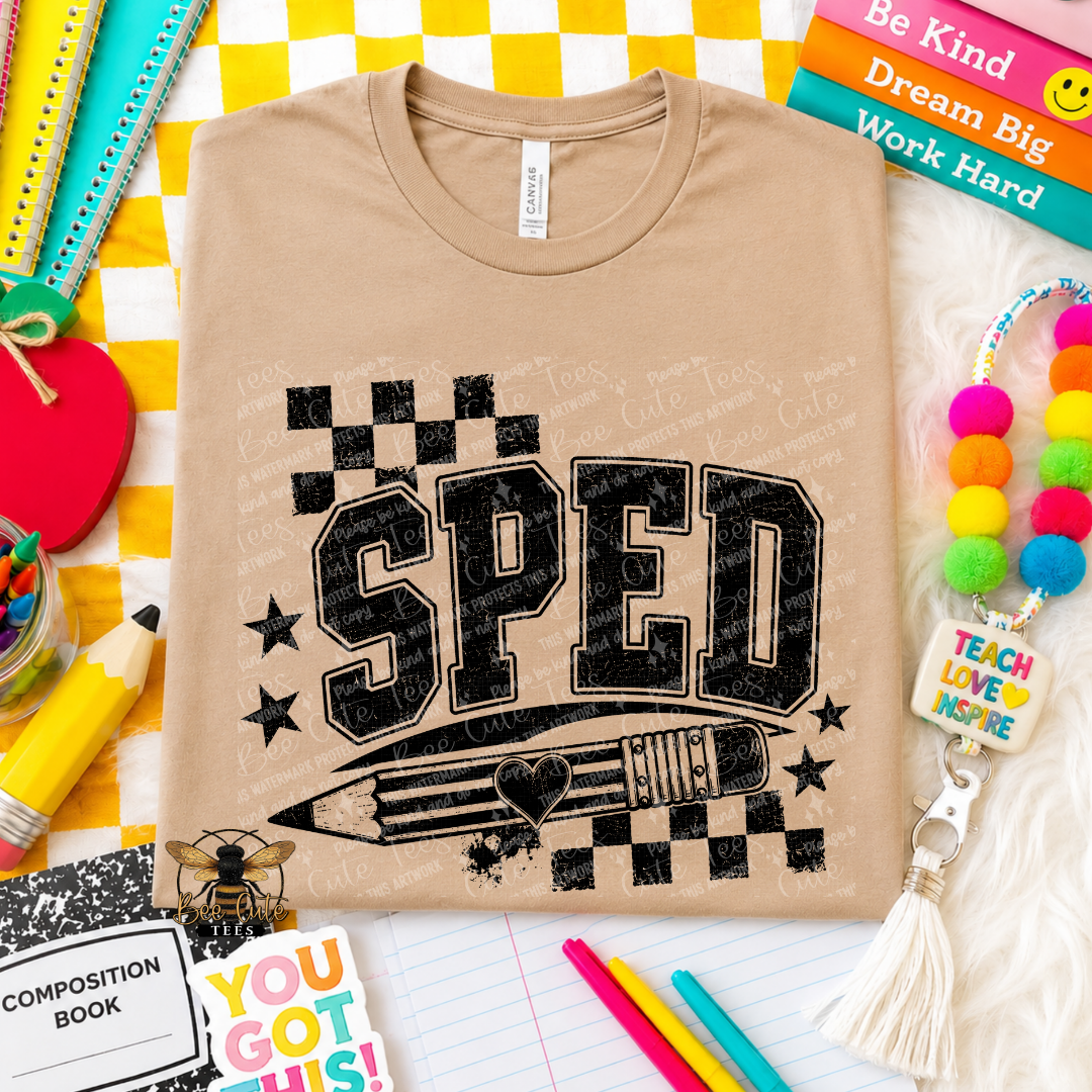 A beige graphic t-shirt featuring the word 'SPED' in distressed black block letters with a pencil and checkered flag design underneath. The shirt is presented in a styled flat-lay composition with school supplies, books, and a pom-pom bracelet.