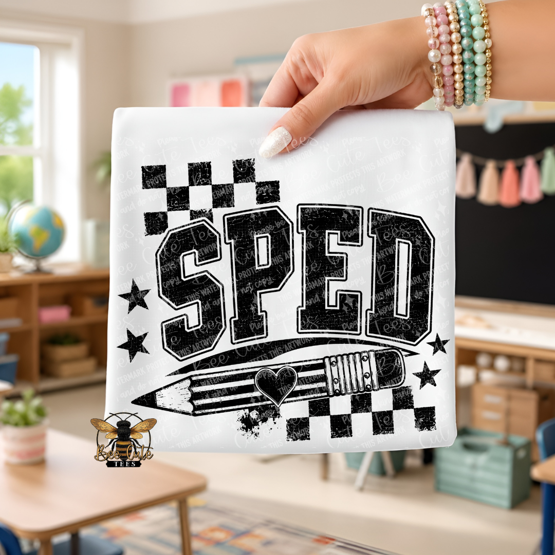 A hand holds a white square fabric item featuring a black distressed graphic that reads “SPED” with stars, checkered flags, and a pencil illustration. The background shows a blurred classroom interior, and a small bee logo appears near the bottom left.