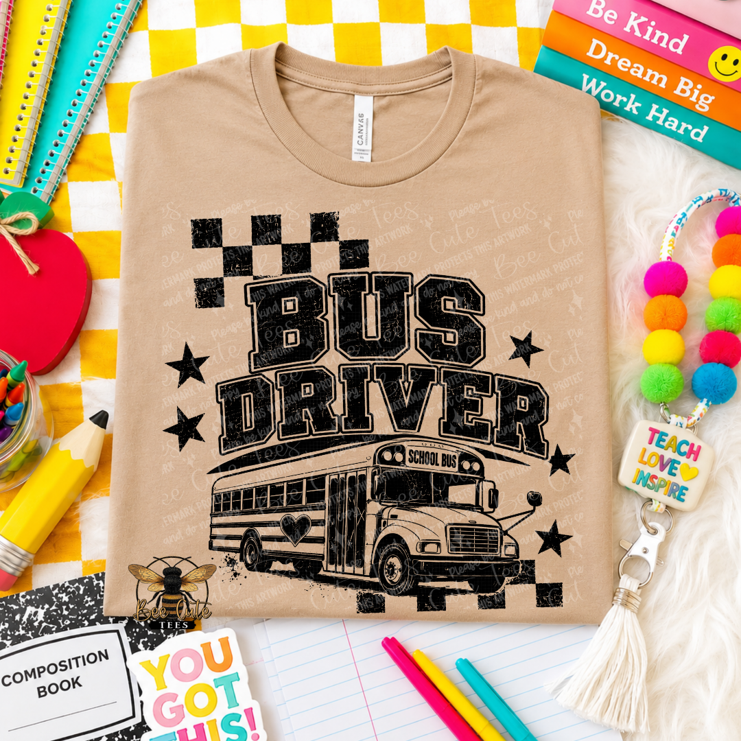 A beige graphic t-shirt featuring a black distressed print that reads 'BUS DRIVER' with a school bus illustration, presented in a styled flat-lay arrangement with school supplies and books.