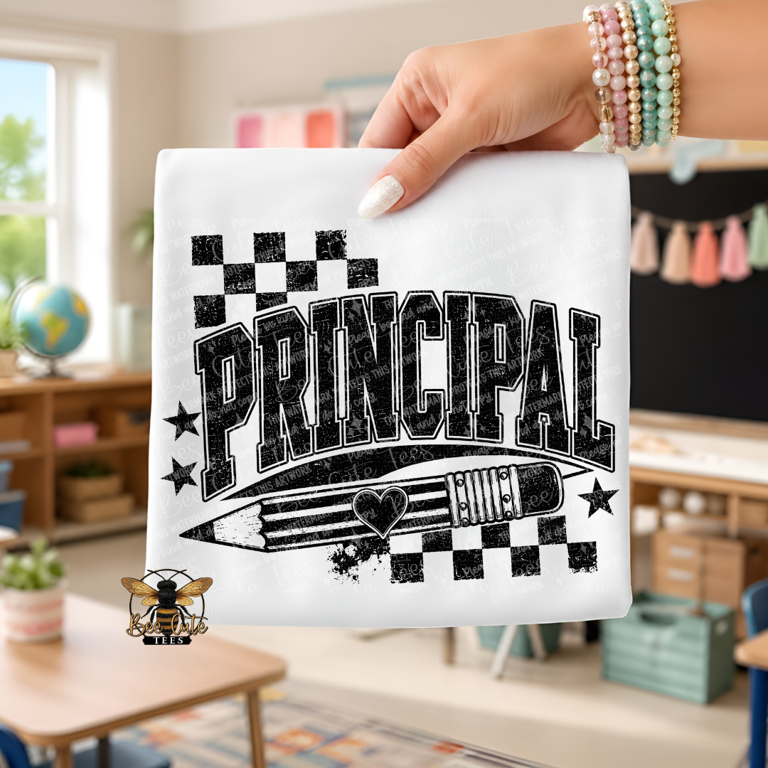 A hand holds up a white t-shirt featuring a black graphic design that reads 'PRINCIPAL' with a pencil, stars, and checkered flags. The background shows a blurred classroom interior.