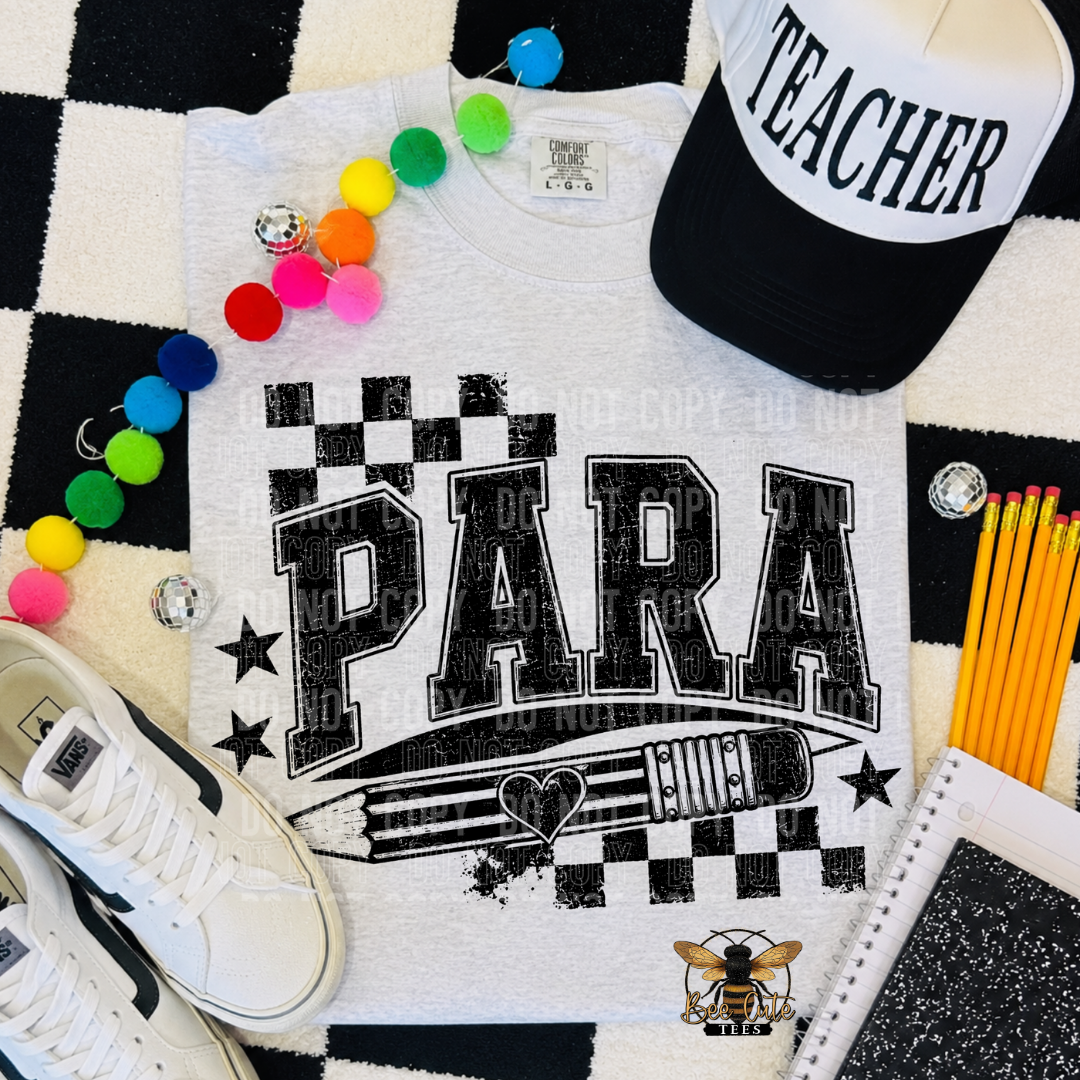A white graphic t-shirt with 'PARA' and a pencil design, styled in a flat lay with a black and white checkered rug, a black and white 'TEACHER' cap, white sneakers, colorful pom-poms, yellow pencils, and a notebook.