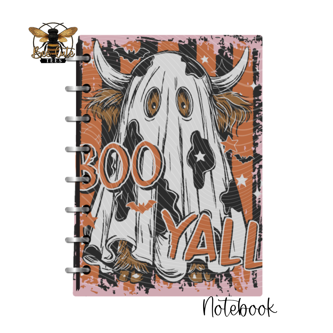 A spiral-bound notebook featuring a Halloween-themed cover illustration of a ghostly cow with the words 'BOO YALL' on a pink, orange, and black distressed background. A bee logo with the text 'BEE CUTE TEES' appears in the top-left corner, and 'Notebook' is written in script at the bottom-right.