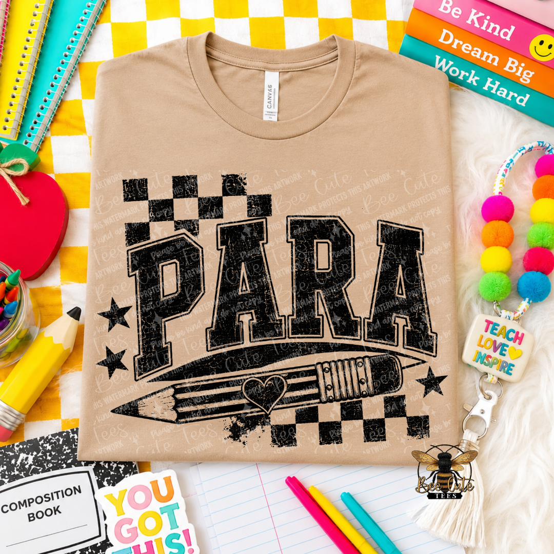 A beige graphic t-shirt featuring the word 'PARA' in distressed black block letters above a black pencil, with a checkerboard pattern and stars. The shirt is displayed in a flat-lay arrangement surrounded by school supplies, books, and a colorful pom-pom keychain.
