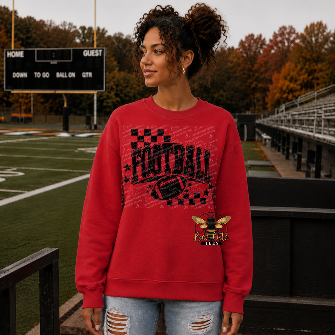 A woman stands on an outdoor sports field wearing a red crewneck sweatshirt with a distressed black and white football graphic and a bee logo that reads 'Bee-Cute TEEs'.