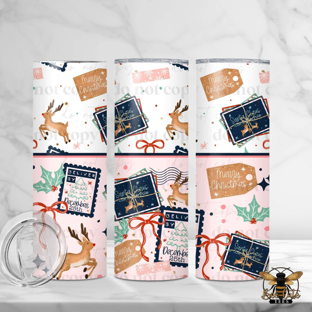 Three tall insulated tumblers with clear lids are shown on a light marble surface. The tumblers have a Christmas-themed wrap design with reindeer, gift boxes, holly leaves, bows, and 'Merry Christmas' tags on a white, pink, and navy background.
