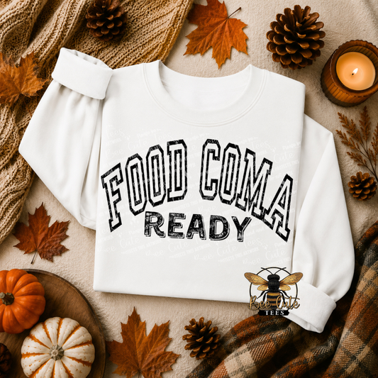 A white long-sleeve sweatshirt with 'FOOD COMA READY' printed in black collegiate-style lettering, styled in an autumn flat lay with pumpkins, pinecones, fall leaves, a knitted scarf, and a candle.