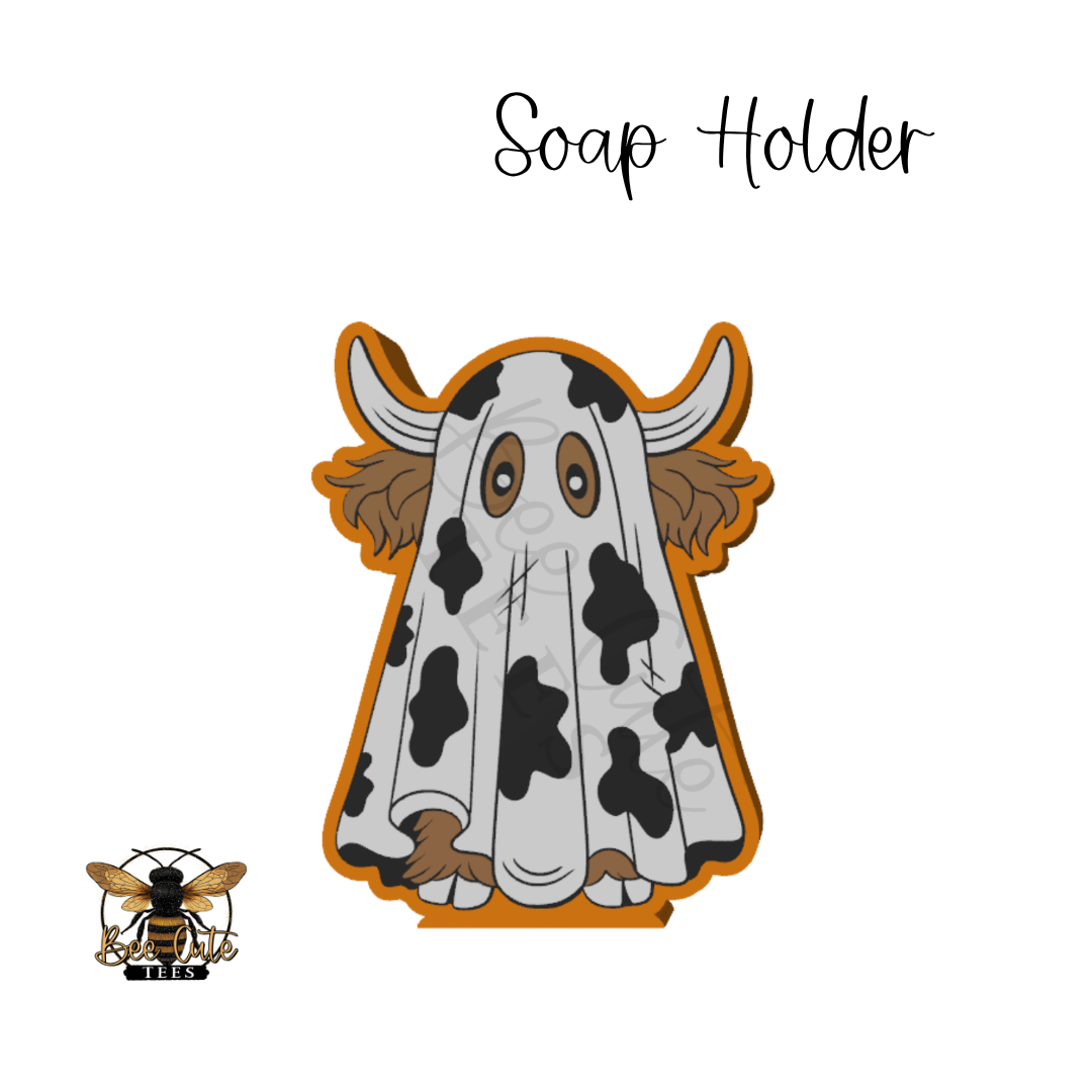 A cartoon-style soap holder shaped like a ghostly cow with horns, featuring a white body with black spots, brown ears and hooves, and an orange border. The words 'Soap Holder' appear above, and a small bee logo with 'Bee Cute Tees' appears in the lower-left corner on a white background.