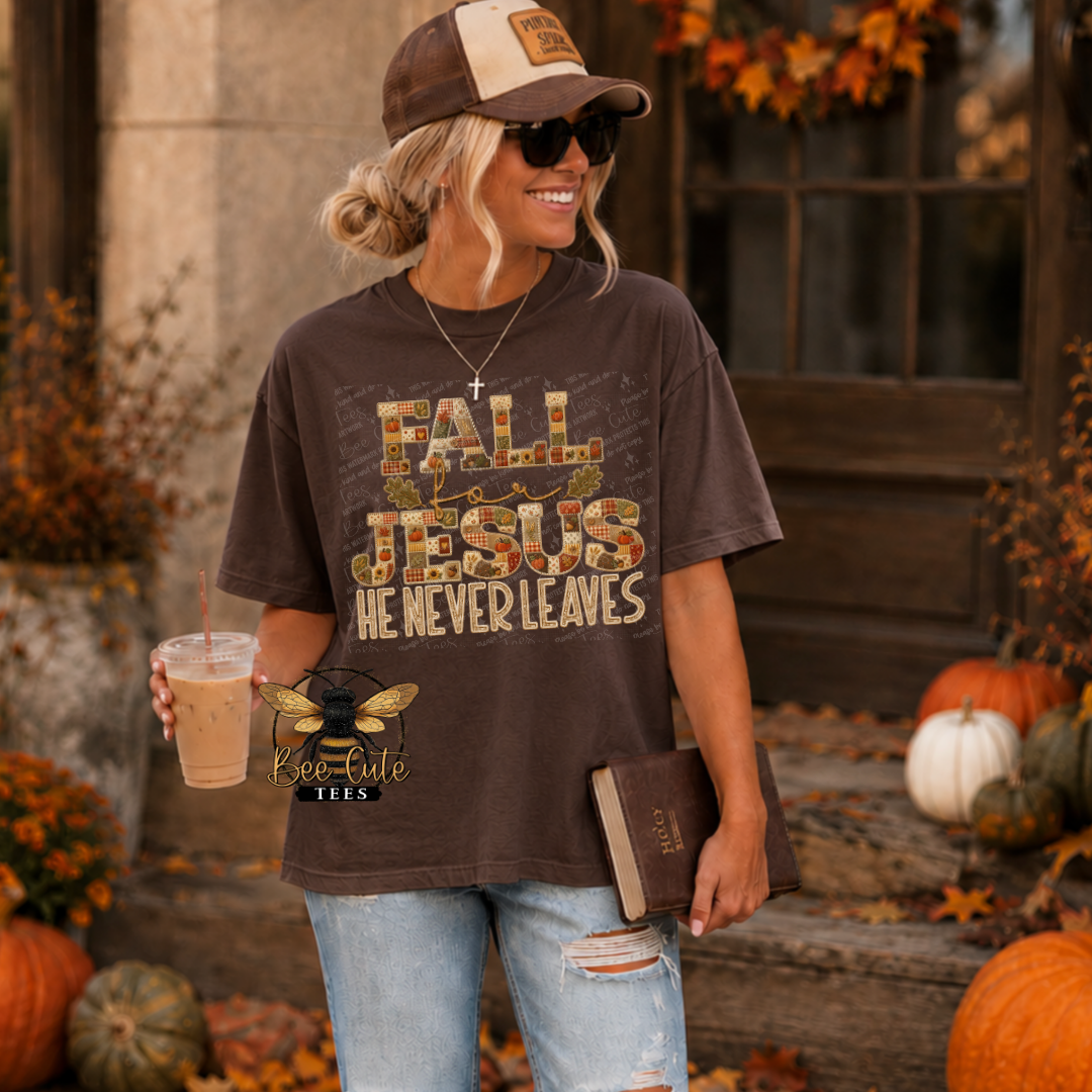 A woman wearing a brown graphic t-shirt with 'FALL JESUS HE NEVER LEAVES' in a distressed autumn pattern, paired with a brown and beige baseball cap and ripped blue jeans. She is holding an iced coffee and a book, standing on a porch decorated with pumpkins and fall leaves.