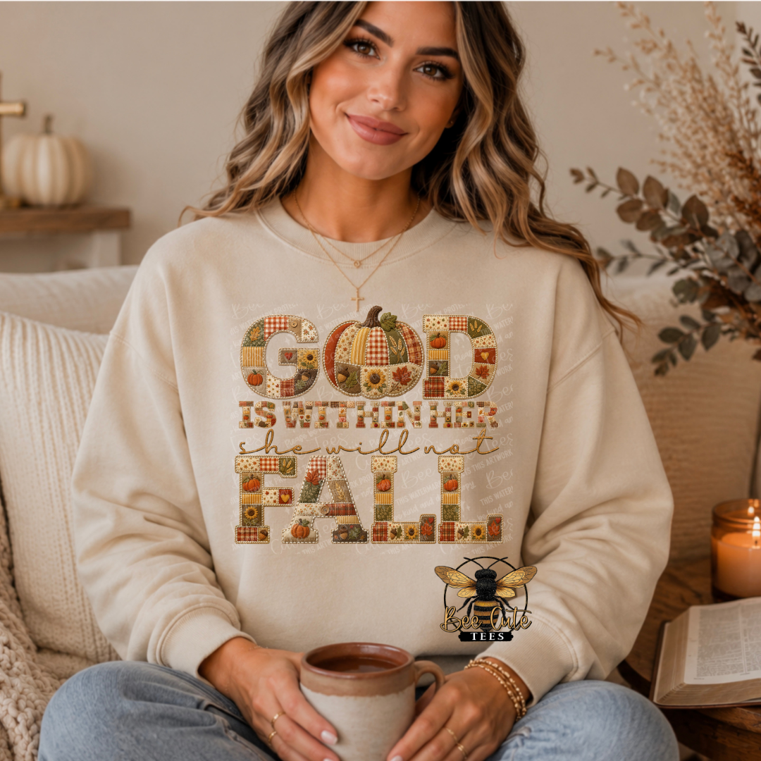 A woman wearing a cream-colored crewneck sweatshirt with a patchwork-style autumn graphic that reads 'GOD IS WITHIN HER she will not FALL' in fall-themed colors. She is holding a mug in a cozy, warmly lit living room setting.