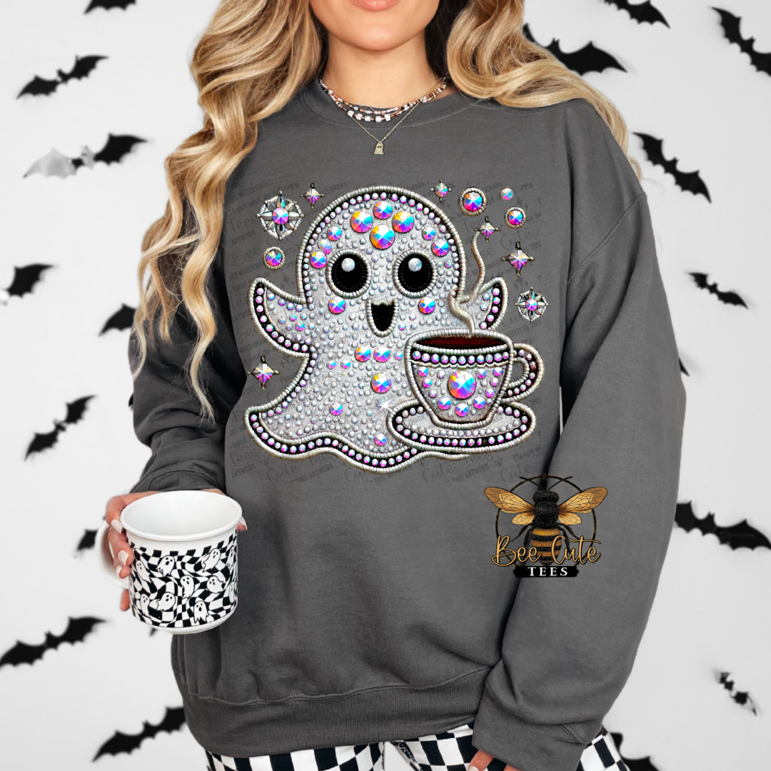 A woman wearing a dark gray crewneck sweatshirt with a large rhinestone-embellished ghost and coffee cup graphic on the front. She is holding a matching black and white patterned mug, with a bee logo visible on the lower right of the sweatshirt.