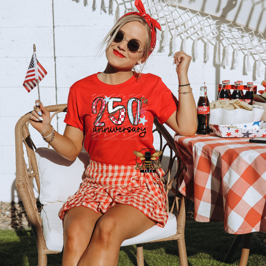 Person wearing a red '250 anniversary' t-shirt and checkered skirt, sitting outdoors with a table of Coca-Cola bottles.