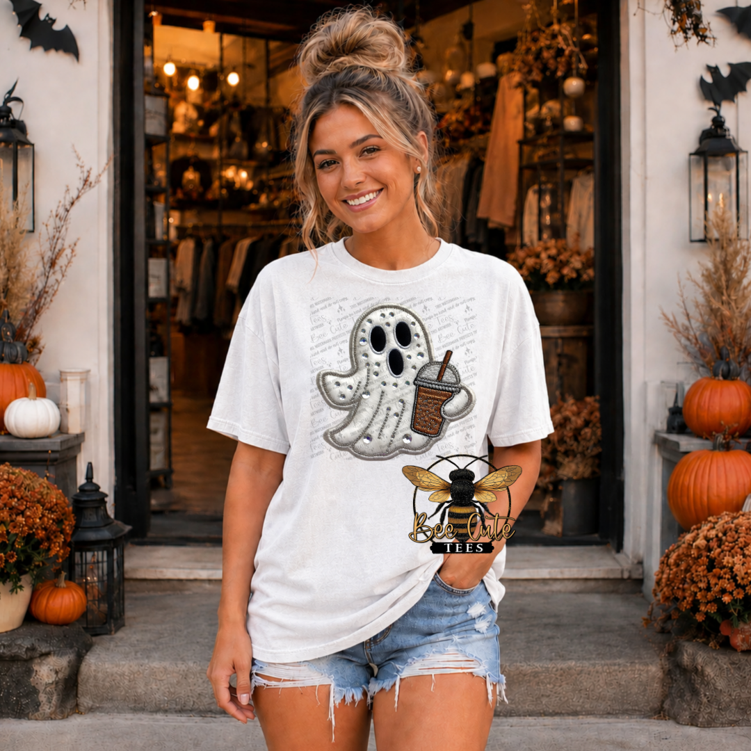A woman stands in front of a storefront wearing an oversized white graphic T-shirt with a ghost holding a coffee cup design and denim shorts. The scene is decorated with pumpkins, fall foliage, and lanterns.