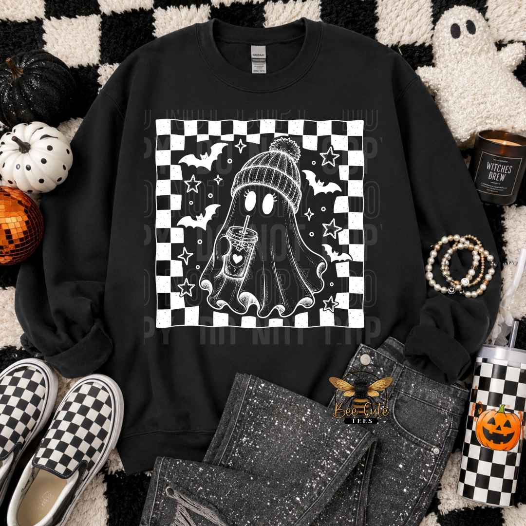 A black crewneck sweatshirt with a white and black checkered graphic of a ghost wearing a beanie and holding a mug, styled in a flat lay with jeans, checkered shoes, a pumpkin, and a candle.