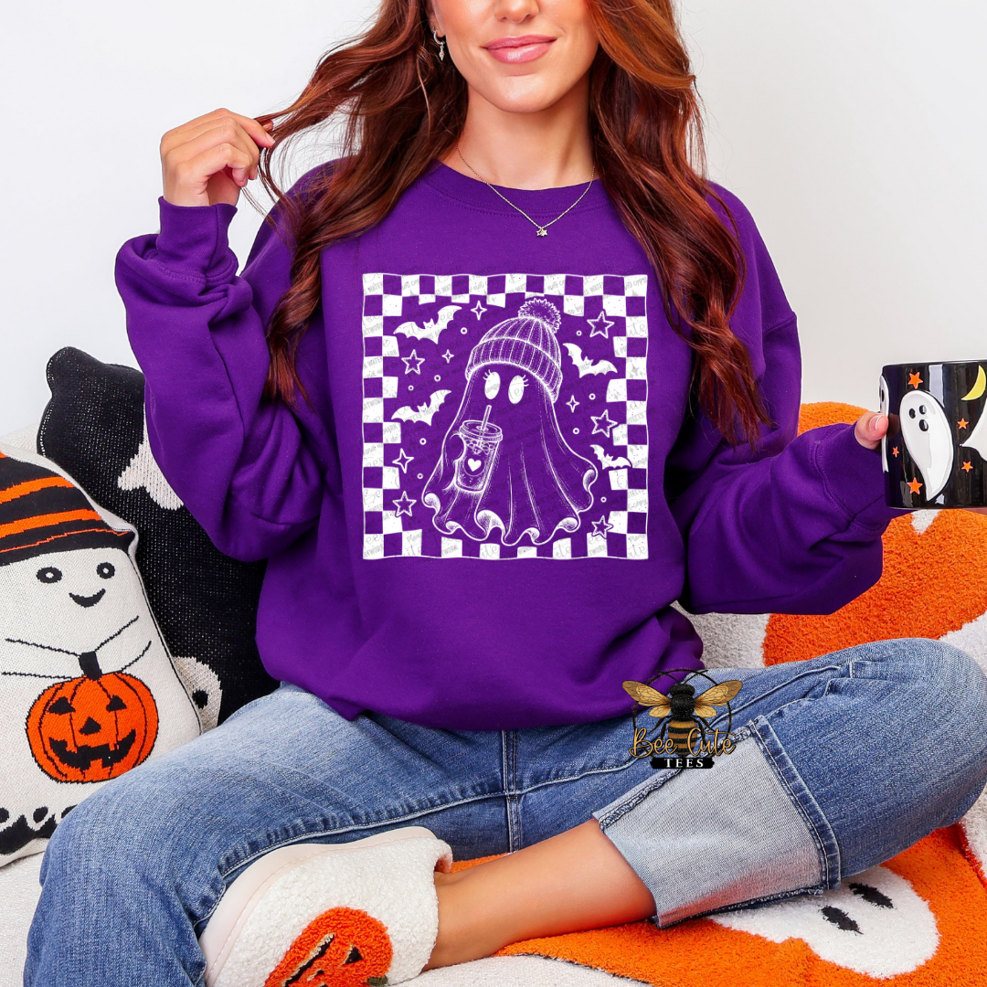 A woman wearing a purple crewneck sweatshirt with a white and purple ghost graphic on the front, sitting on an orange and white blanket with a black cat pillow.