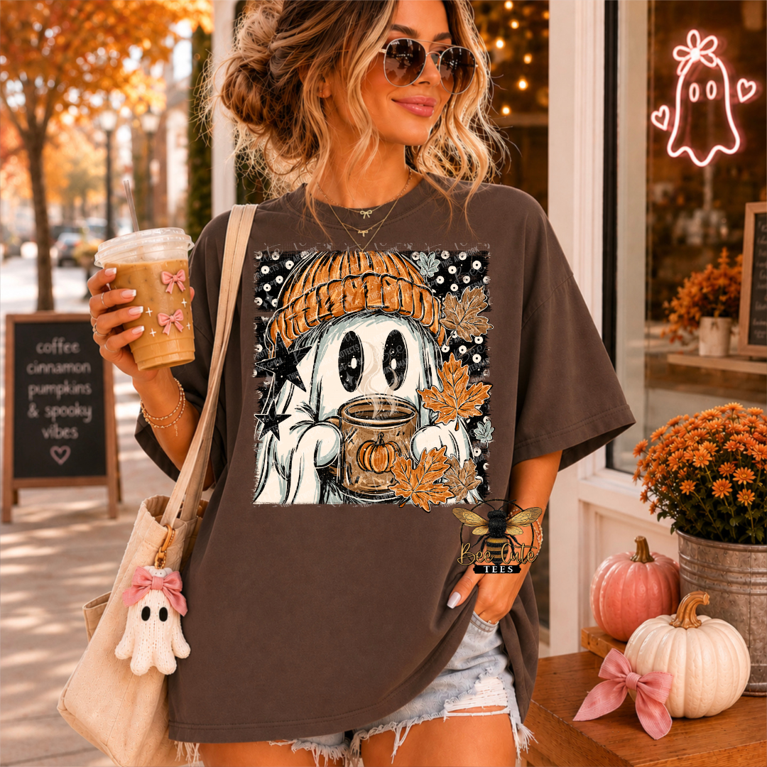 A woman wearing a dark brown oversized t-shirt with a graphic of a cute cartoon ghost in a beanie holding a coffee mug, set against a cozy autumn storefront background.