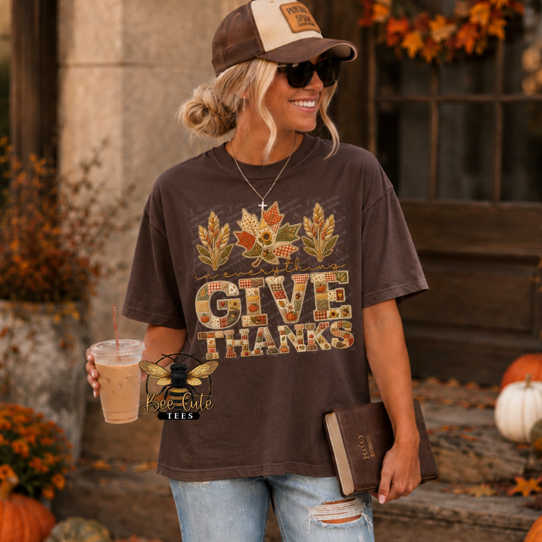 A woman wearing a brown graphic t-shirt with a 'GIVE THANKS' autumn leaf design, styled with a baseball cap, sunglasses, and jeans in an outdoor fall-themed setting.