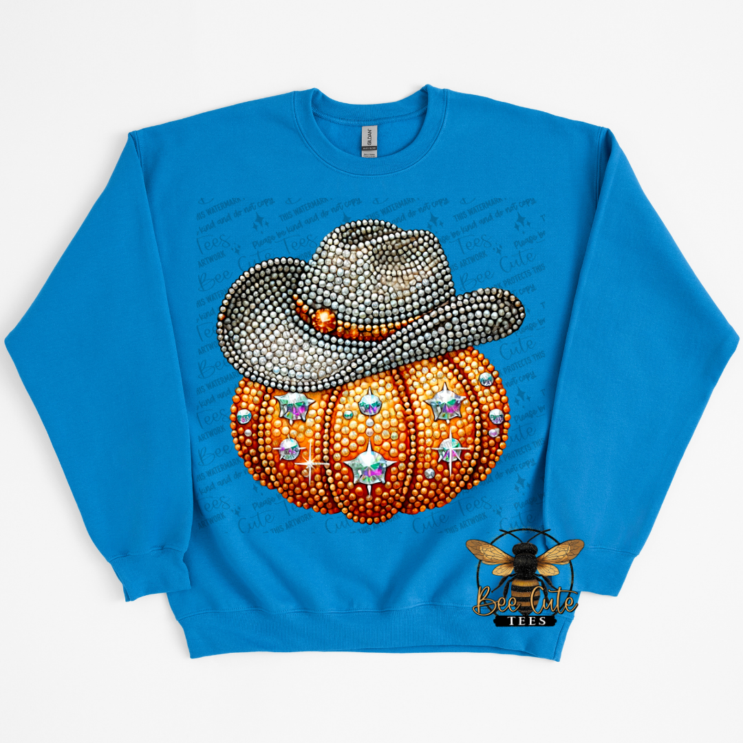 A bright blue crewneck sweatshirt featuring a rhinestone-style graphic of an orange pumpkin topped with a silver cowboy hat, with a bee logo near the lower right hem.