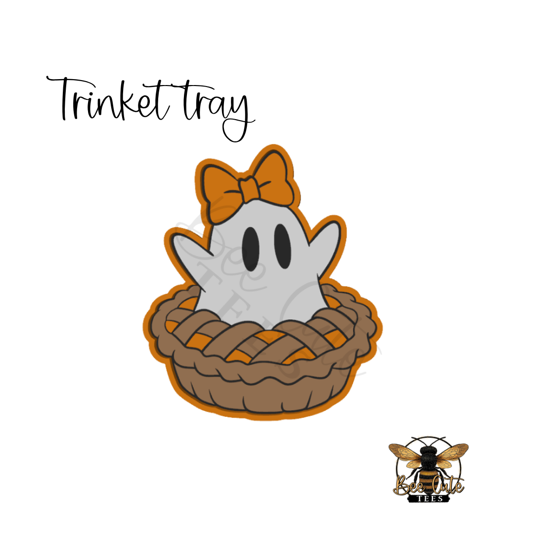 A cute cartoon ghost sitting in a woven brown pie with an orange bow, shown on a white background with the text 'Trinket tray' and a small bee logo in the lower right.