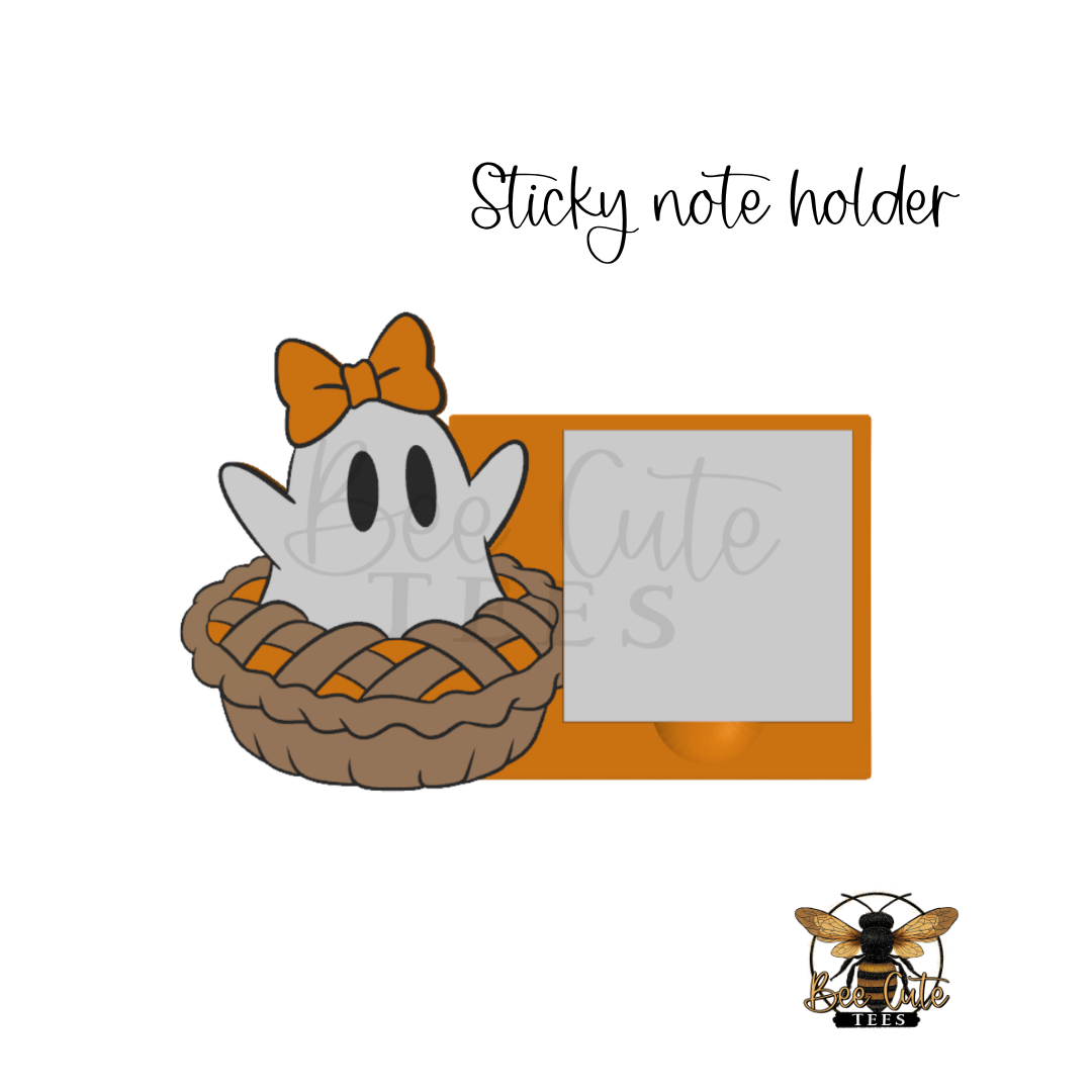 A cute Halloween-themed sticky note holder featuring a white cartoon ghost wearing an orange bow sitting in a pie crust, next to an orange rectangular frame with a blank photo slot. The text 'Sticky note holder' is written above, and a bee logo for 'Cute Stickers' appears in the bottom right corner.