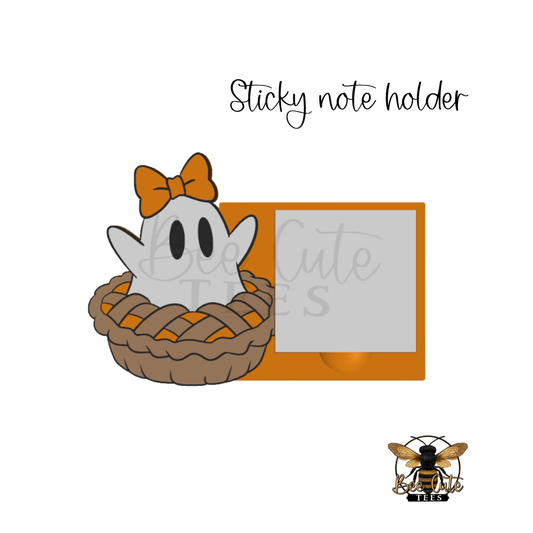 A cute Halloween-themed sticky note holder featuring a white cartoon ghost wearing an orange bow sitting in a pie crust, next to an orange rectangular frame with a blank photo slot. The text 'Sticky note holder' is written above, and a bee logo for 'Cute Stickers' appears in the bottom right corner.