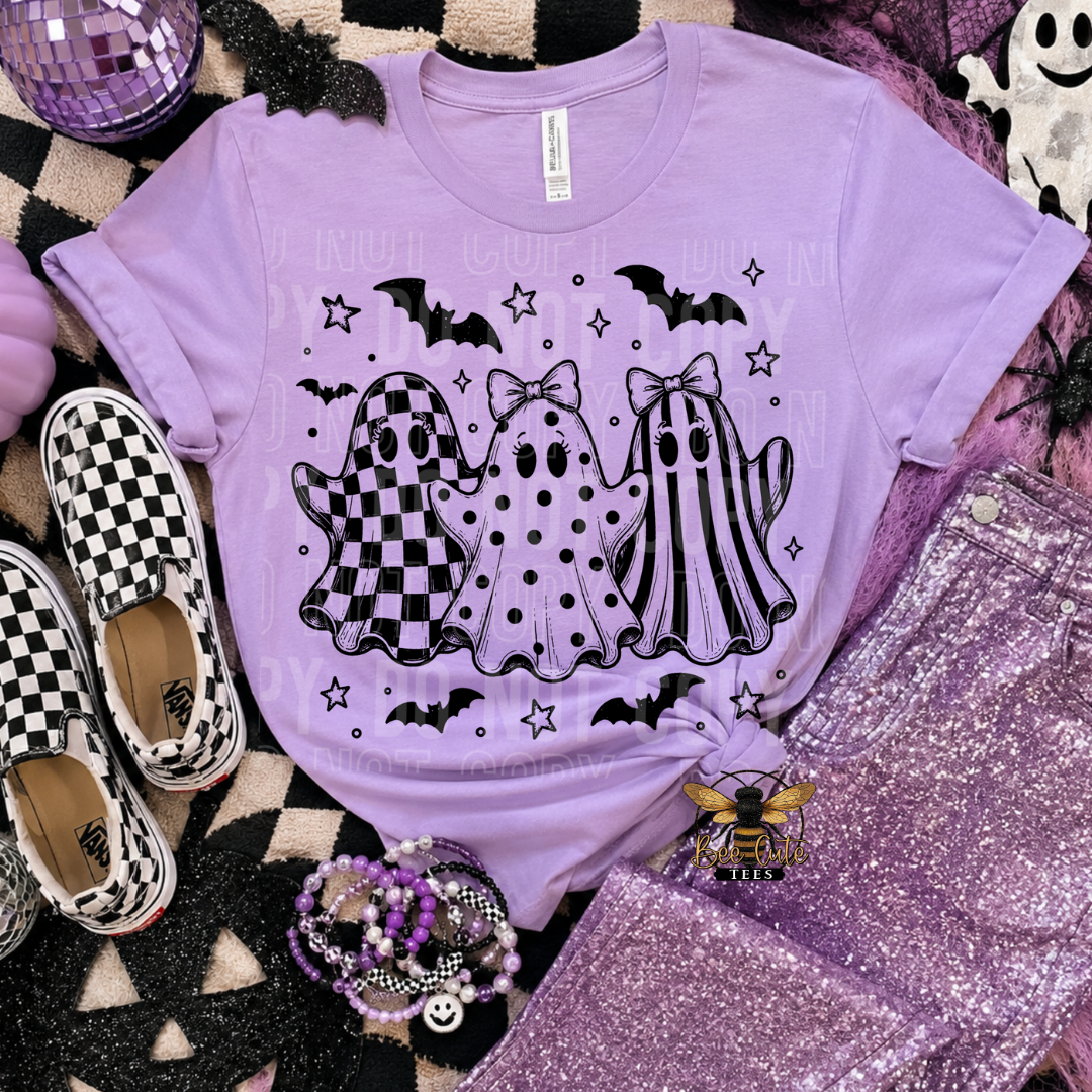 A lavender purple short-sleeve t-shirt with a black and white Halloween graphic of three ghosts, displayed in a flat-lay arrangement with purple glitter pants, checkerboard slip-on shoes, and a black-and-white checkered blanket.