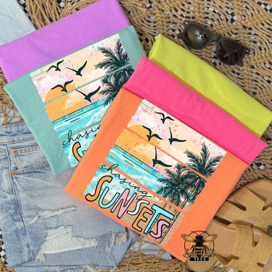 Colorful t-shirts with sunset design and 'chasing sunsets' text on a textured surface.