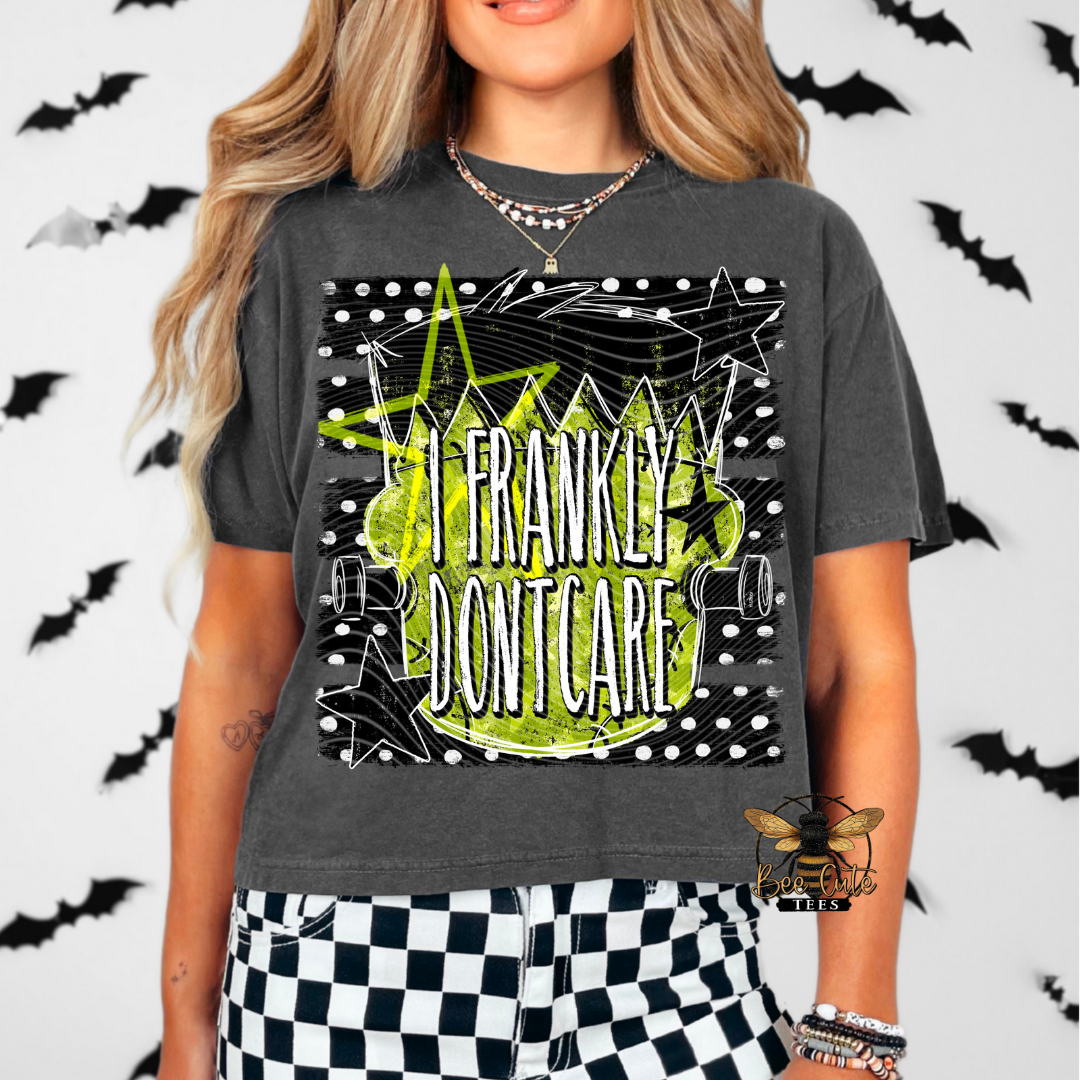A woman wearing a dark gray graphic t-shirt with a lime green and white 'I FRANKLY DONT CARE' design, paired with black and white checkered pants, set against a white background with black bat silhouettes.