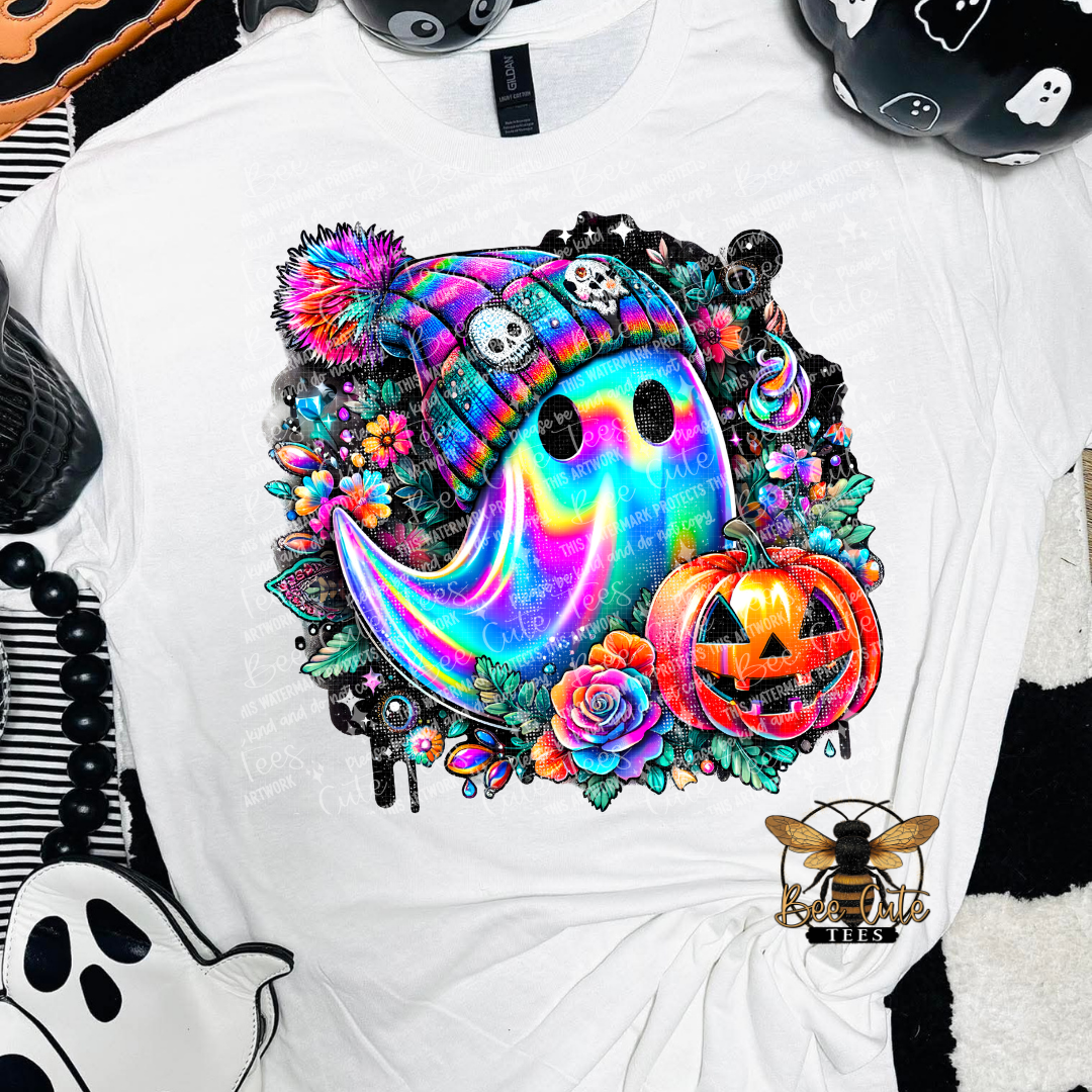 A white short-sleeve t-shirt featuring a vibrant, colorful graphic of a ghost in a rainbow-striped beanie surrounded by a Halloween-themed design with a jack-o'-lantern, roses, skulls, and candy. The shirt is styled with other black-and-white Halloween-themed items.