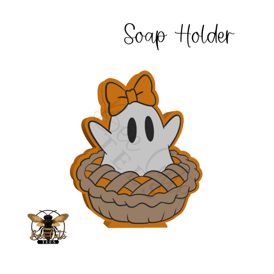 A cartoon-style soap holder featuring a white ghost with black eyes and a brown bow, sitting in a brown woven pie with an orange outline, on a white background. The text 'Soap Holder' appears above, and a bee logo with 'BEE' is in the lower-left corner.