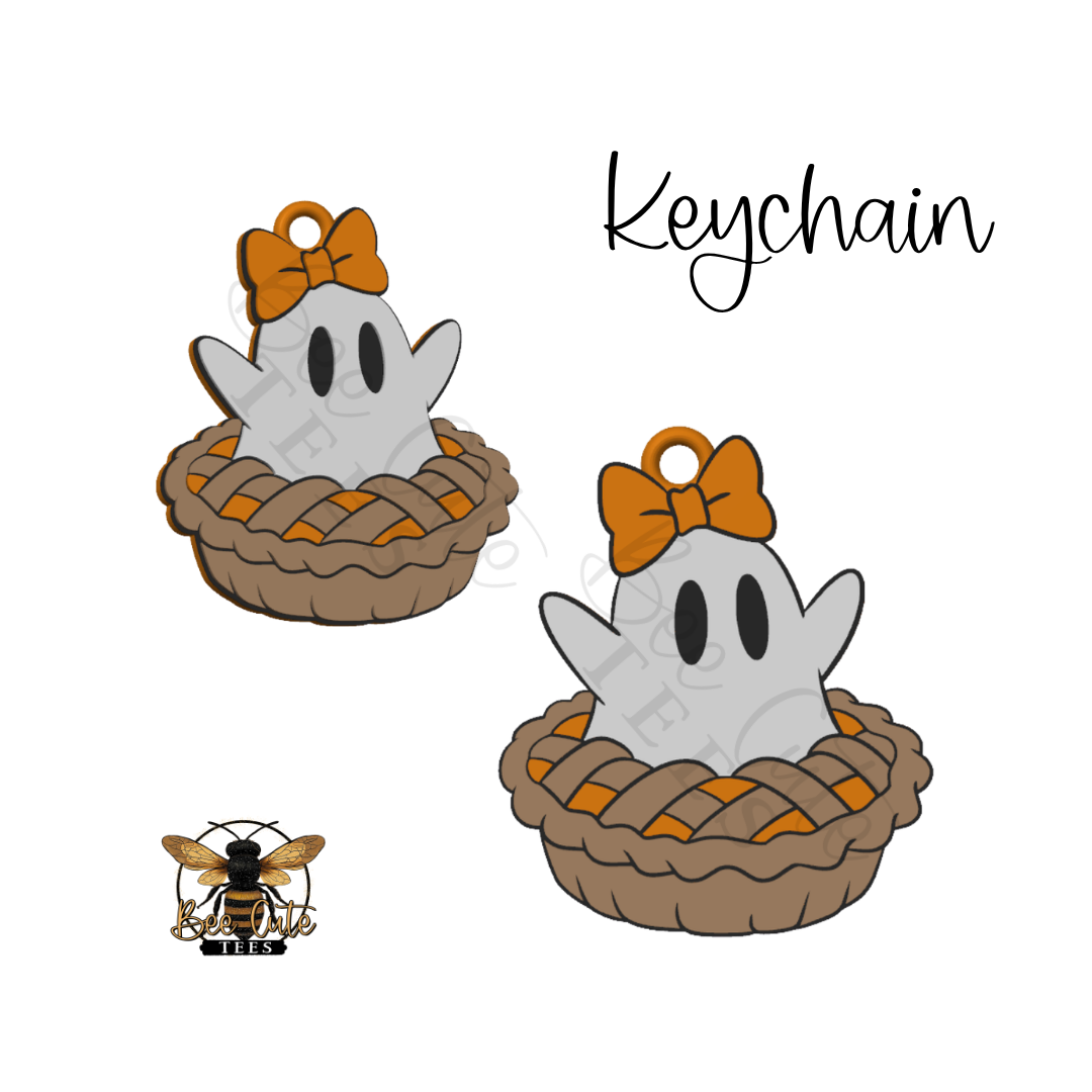 A digital graphic design of a cute cartoon ghost keychain nestled in a brown pie crust, featuring an orange bow on its head. The image shows two variations of the keychain, the word 'Keychain' written in script, and a small bee logo in the bottom-left corner, all on a solid white background.