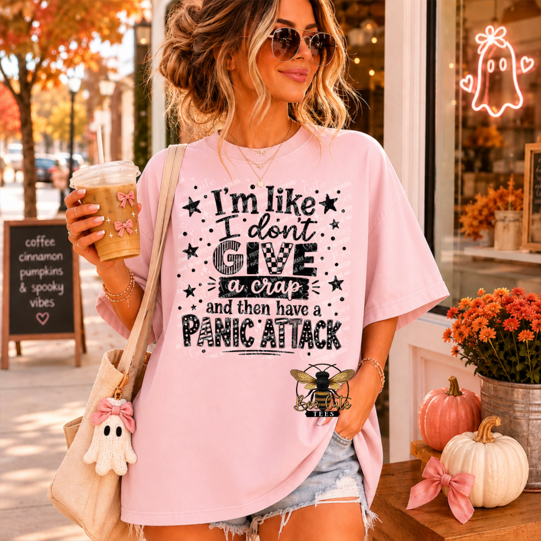 A woman wearing a light pink graphic t-shirt with a black text design that reads 'I'm like I don't GIVE a crap and then have a PANIC ATTACK' with a bee logo at the bottom, standing in a storefront.