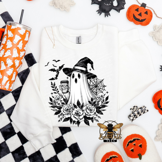 A white long-sleeve sweatshirt with a black and white Halloween graphic of a ghost, witch hat, spiderwebs, roses, and bats, styled in a flat lay with seasonal props.