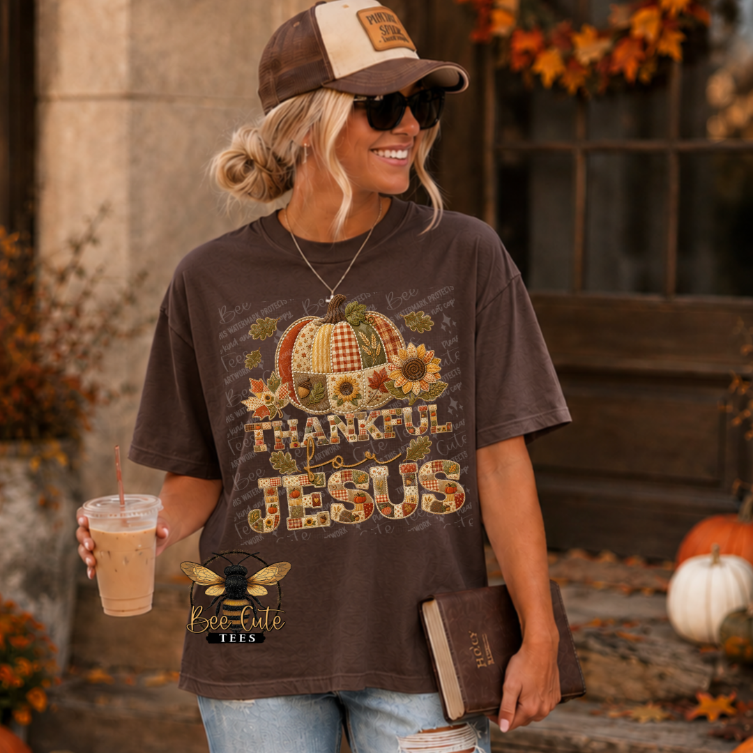 A woman wearing a brown graphic t-shirt with a 'Thankful Jesus' pumpkin design, styled with a baseball cap, sunglasses, and jeans in an autumn-themed outdoor setting.