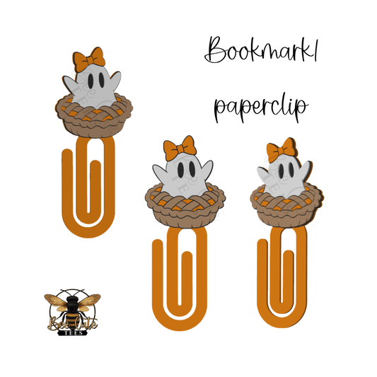 Three ghost-themed paperclips on a white background, each with a white ghost wearing an orange bow and sitting in a brown pie, attached to a large orange paperclip. Handwritten text reads 'Bookmark paperclip,' and a bee logo appears in the lower left.